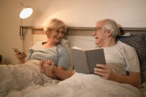 Professional overnight carer in blue uniform adjusting bedding for an elderly man in a home bedroom setting