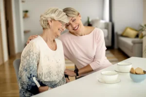 An older woman shares morning tea with her live-in carer at home in London, reflecting warm, person-centred dementia care