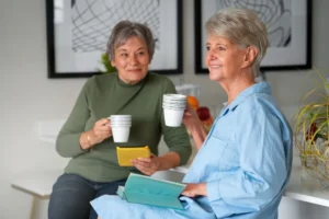 Two older women discuss 24-hour live-in care costs over tea in a bright London kitchen
