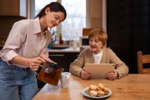 Home carer pouring tea for an elderly woman at her kitchen table during an evening care visit in London